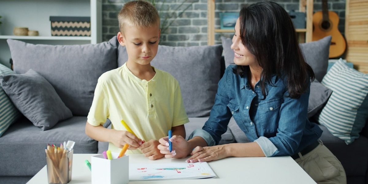 Young family mom and son are drawing with markers in apartment talking smiling relaxing in living room together. Lifestyle, people and parenting concept.