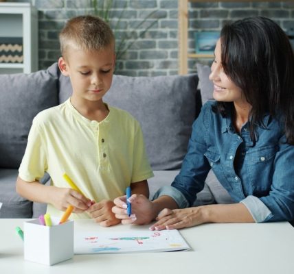 Young family mom and son are drawing with markers in apartment talking smiling relaxing in living room together. Lifestyle, people and parenting concept.